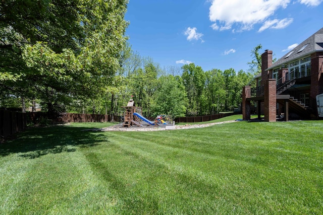 view of yard featuring a playground, a fenced backyard, and stairs