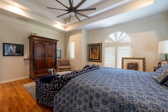 bedroom with a raised ceiling, multiple windows, visible vents, and wood finished floors