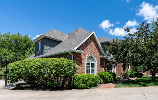 view of side of property with a shingled roof and brick siding