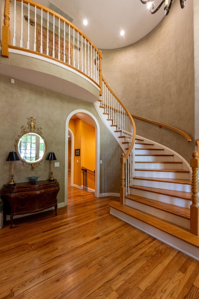staircase featuring recessed lighting, visible vents, wood finished floors, arched walkways, and a high ceiling