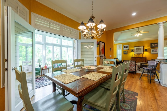 dining space featuring decorative columns, crown molding, light wood-style flooring, and ceiling fan with notable chandelier