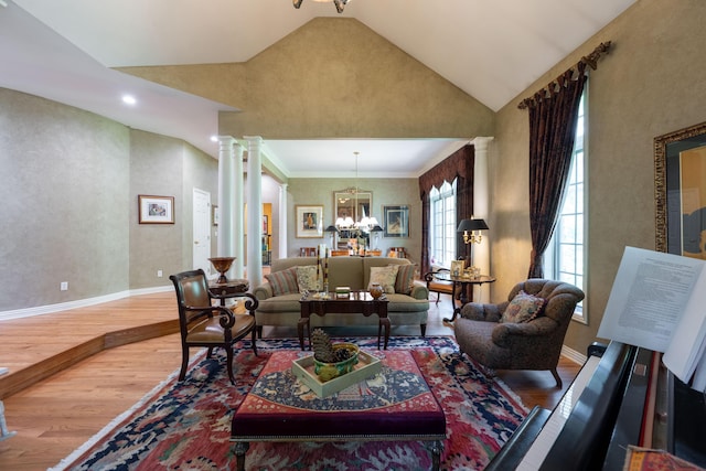 living area with wood finished floors, ornate columns, a notable chandelier, baseboards, and vaulted ceiling