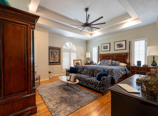 bedroom featuring a tray ceiling, light wood-style flooring, a ceiling fan, and ornamental molding