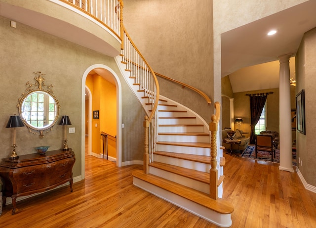stairs with arched walkways, a healthy amount of sunlight, a high ceiling, and wood finished floors