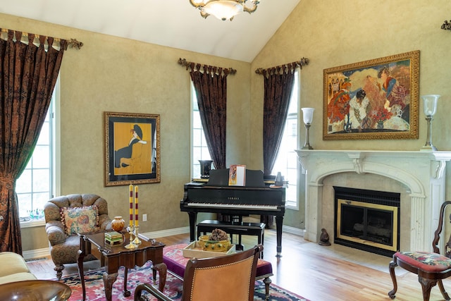 living area with baseboards, wood finished floors, lofted ceiling, and a fireplace with flush hearth