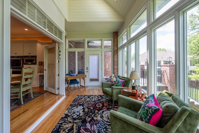 sunroom featuring a towering ceiling, plenty of natural light, and wood finished floors