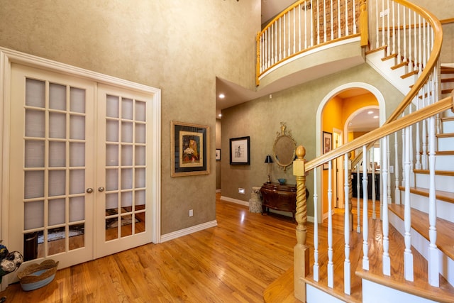 entryway with french doors, wood finished floors, a high ceiling, arched walkways, and stairs
