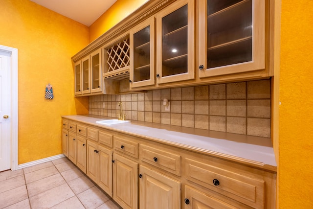kitchen featuring a sink, light tile patterned flooring, light countertops, glass insert cabinets, and baseboards