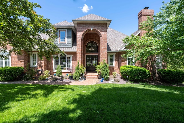 view of front of property featuring roof with shingles, a front lawn, a chimney, and brick siding