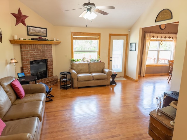 living area with lofted ceiling, a fireplace, light wood-type flooring, and a ceiling fan