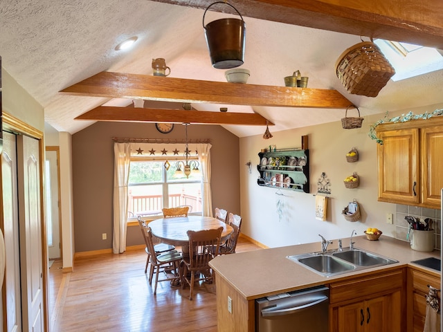 kitchen featuring a peninsula, a sink, vaulted ceiling with skylight, dishwasher, and light wood-style floors