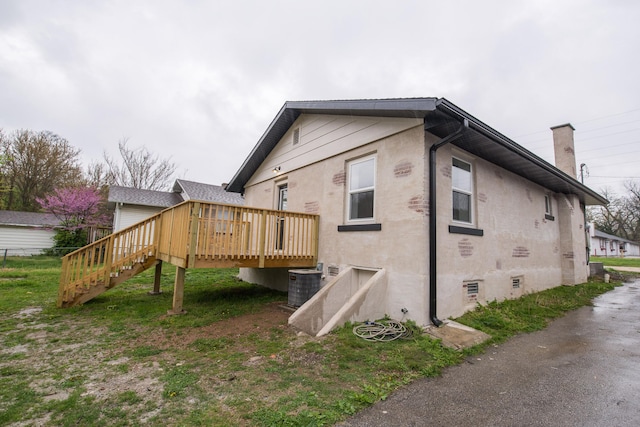 view of side of property with cooling unit, stucco siding, stairway, and a wooden deck