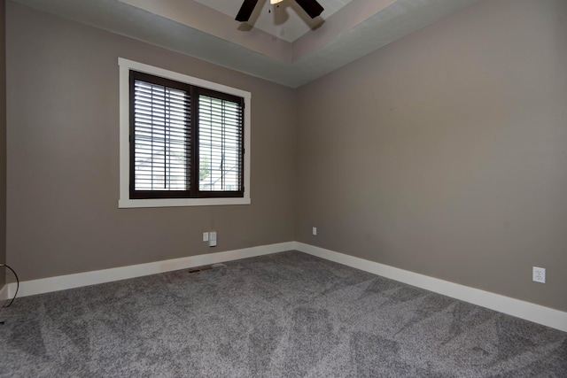 unfurnished room featuring baseboards, dark colored carpet, ceiling fan, and a tray ceiling