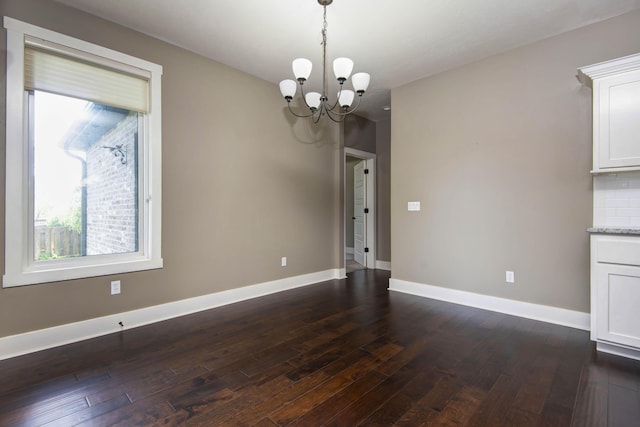 unfurnished dining area featuring an inviting chandelier, dark wood-type flooring, and baseboards