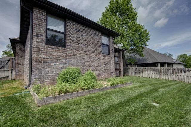 view of side of property with a yard, fence, a garden, and brick siding