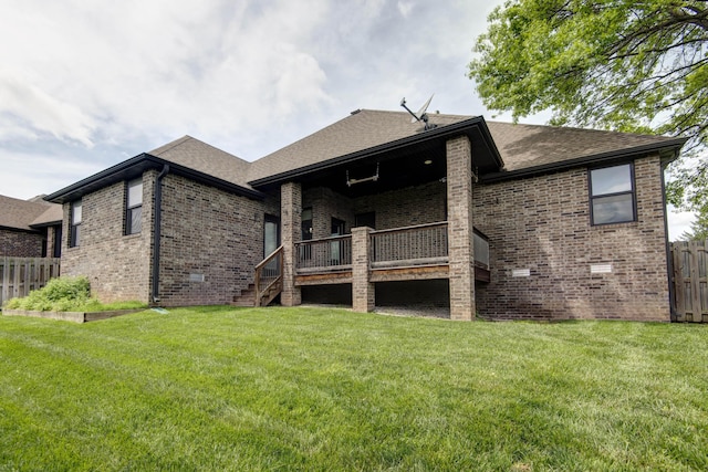 rear view of property with a yard, brick siding, roof with shingles, and fence