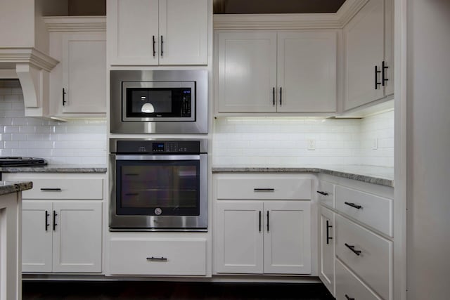 kitchen featuring white cabinets, stainless steel appliances, tasteful backsplash, and light stone countertops