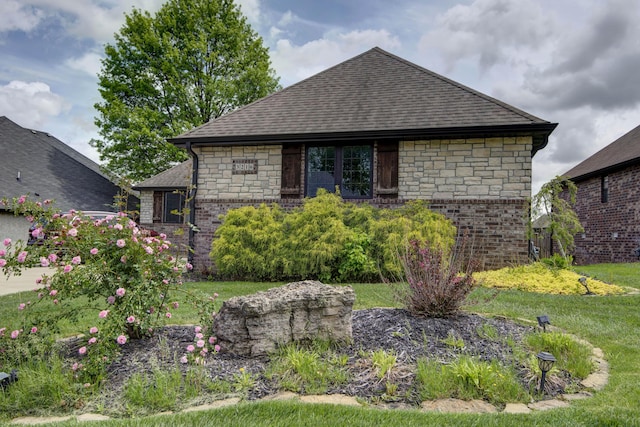 view of front of house featuring stone siding, roof with shingles, and a front lawn