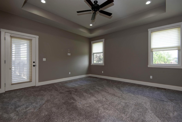 unfurnished room featuring a tray ceiling, dark colored carpet, and baseboards