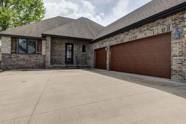 view of front of home featuring roof with shingles, concrete driveway, a garage, and brick siding