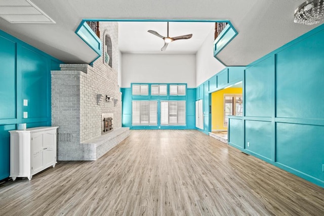 unfurnished living room featuring a brick fireplace, a high ceiling, a ceiling fan, and wood finished floors