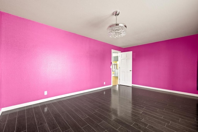 spare room featuring wood finished floors, baseboards, and a notable chandelier