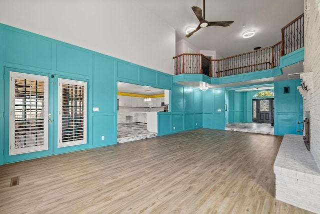 unfurnished living room featuring wood finished floors, visible vents, a decorative wall, a towering ceiling, and ceiling fan