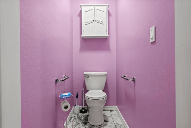 half bathroom featuring toilet, marble finish floor, baseboards, and a textured wall