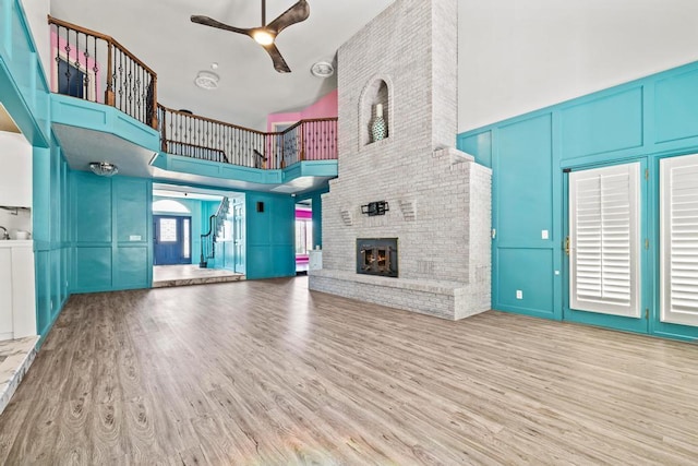 unfurnished living room featuring a ceiling fan, a decorative wall, a towering ceiling, wood finished floors, and a fireplace