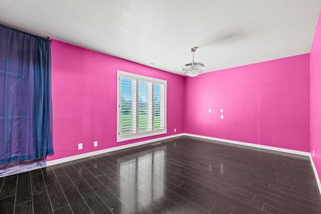 spare room featuring baseboards, a notable chandelier, and wood finished floors