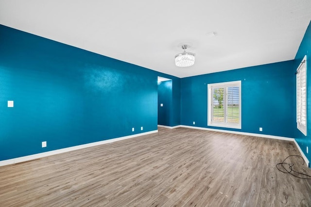 unfurnished room featuring wood finished floors, baseboards, and a notable chandelier