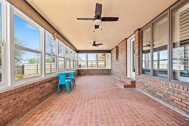 unfurnished sunroom with brick wall, ceiling fan, and brick floor