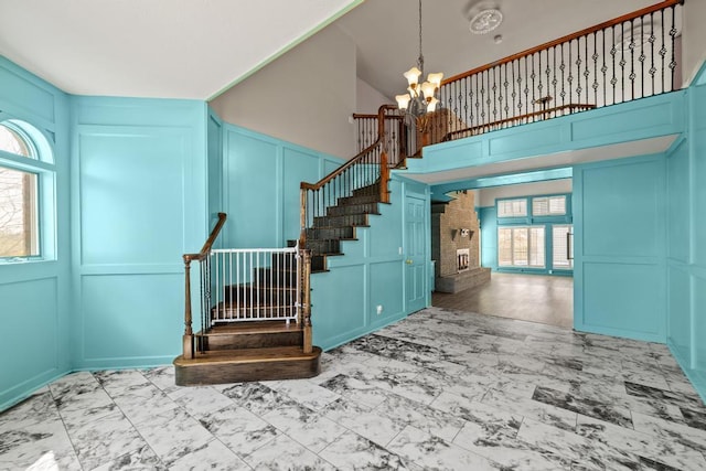 stairway featuring marble finish floor, a decorative wall, a chandelier, and a high ceiling