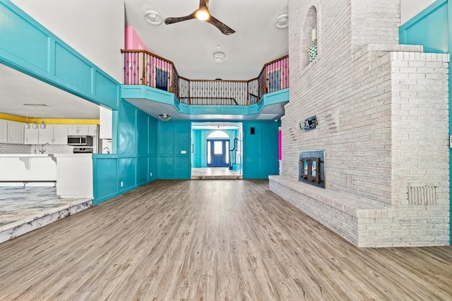 unfurnished living room with ceiling fan, light wood-type flooring, a brick fireplace, and a high ceiling