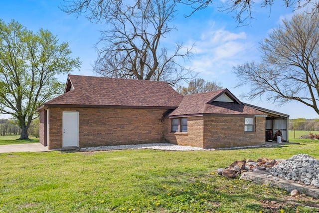 view of side of property featuring a yard, brick siding, and roof with shingles