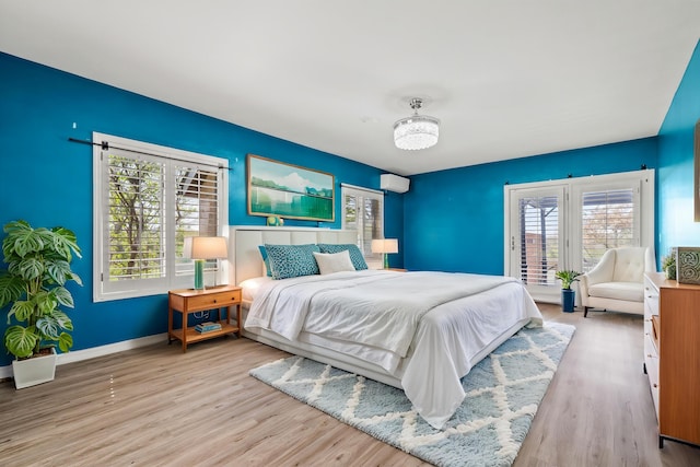 bedroom featuring wood finished floors, an AC wall unit, baseboards, and multiple windows