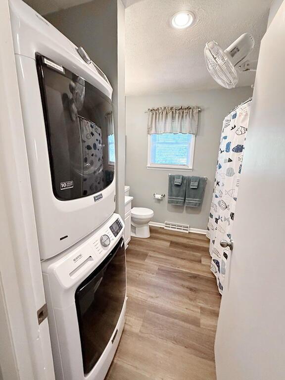 full bath with stacked washer / dryer, a textured ceiling, toilet, visible vents, and wood finished floors