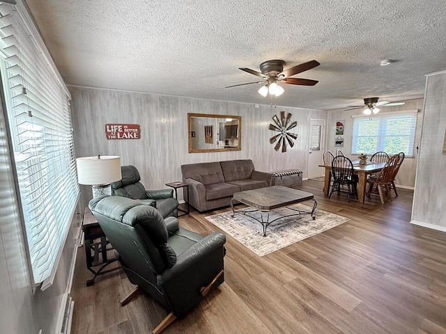 living area featuring a ceiling fan, baseboards, a textured ceiling, and wood finished floors