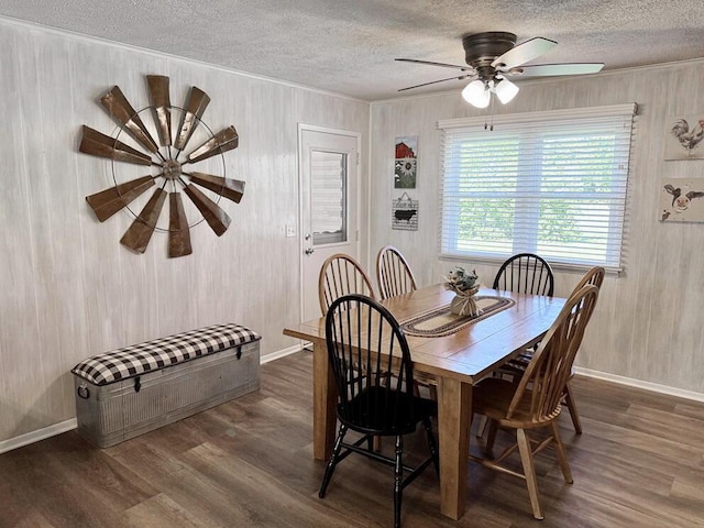 dining space featuring a textured ceiling, wooden walls, baseboards, and dark wood-style floors
