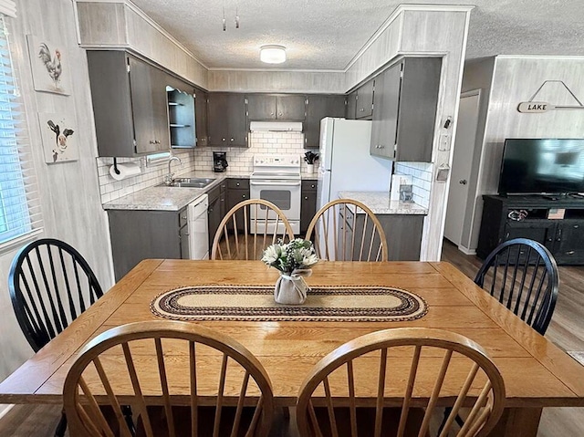kitchen featuring a textured ceiling, white appliances, a sink, wood finished floors, and light countertops