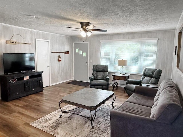 living room with wooden walls, a textured ceiling, a ceiling fan, and wood finished floors