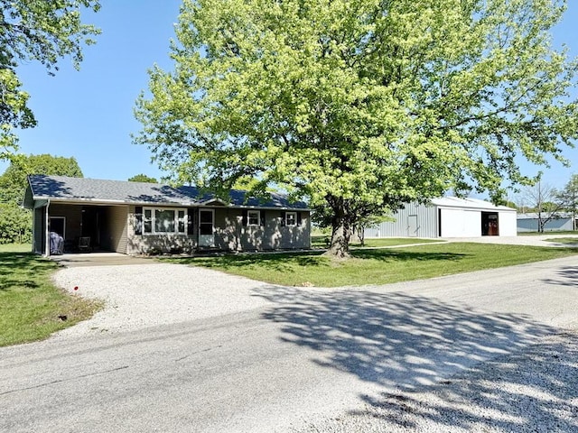 ranch-style home featuring a garage, a front lawn, an outbuilding, and driveway