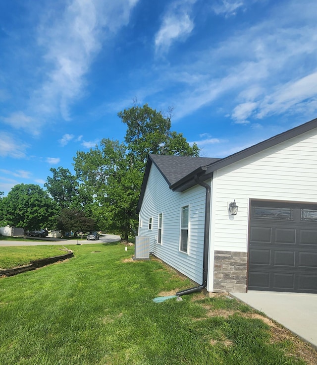 view of side of home featuring a yard, a garage, a shingled roof, and stone siding
