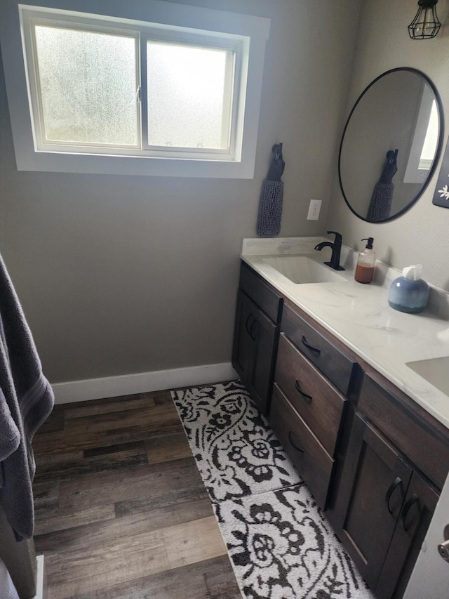 bathroom with a sink, double vanity, baseboards, and wood finished floors