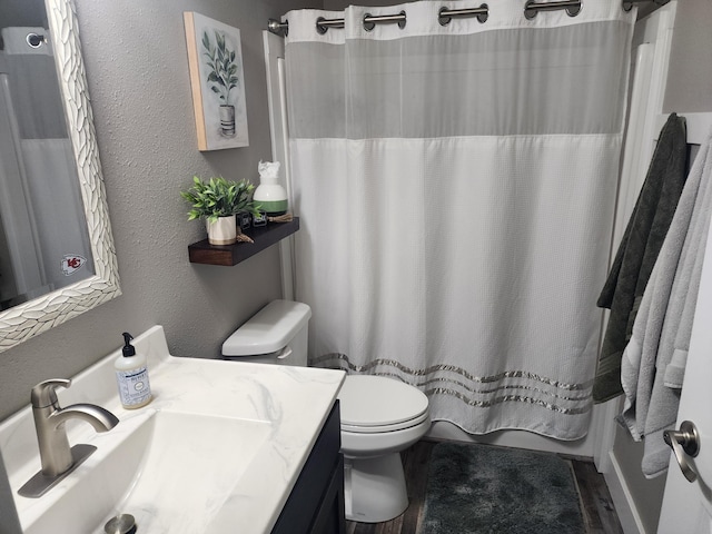 bathroom with toilet, wood finished floors, vanity, and a textured wall