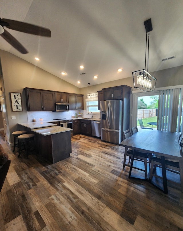 kitchen featuring a peninsula, stainless steel appliances, lofted ceiling, dark wood finished floors, and hanging light fixtures