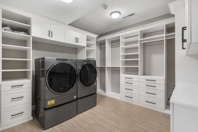 clothes washing area featuring wood finish floors, washing machine and dryer, visible vents, and cabinet space