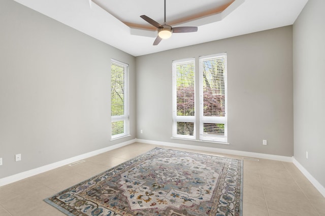 empty room featuring light tile patterned floors, a raised ceiling, a ceiling fan, and a healthy amount of sunlight