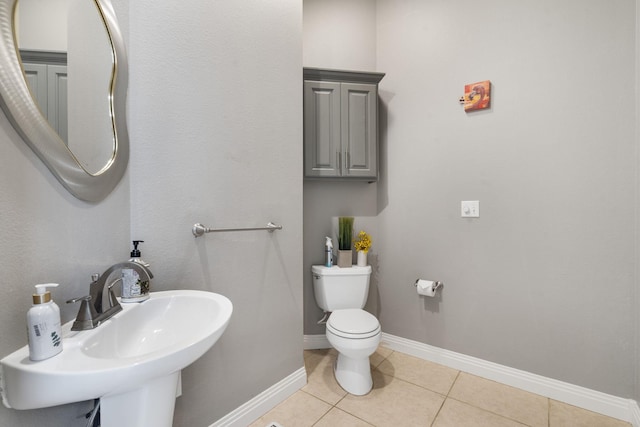 bathroom featuring toilet, baseboards, tile patterned floors, and a sink