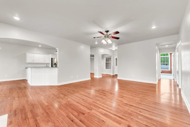 unfurnished living room with light wood-style floors, baseboards, a ceiling fan, and arched walkways